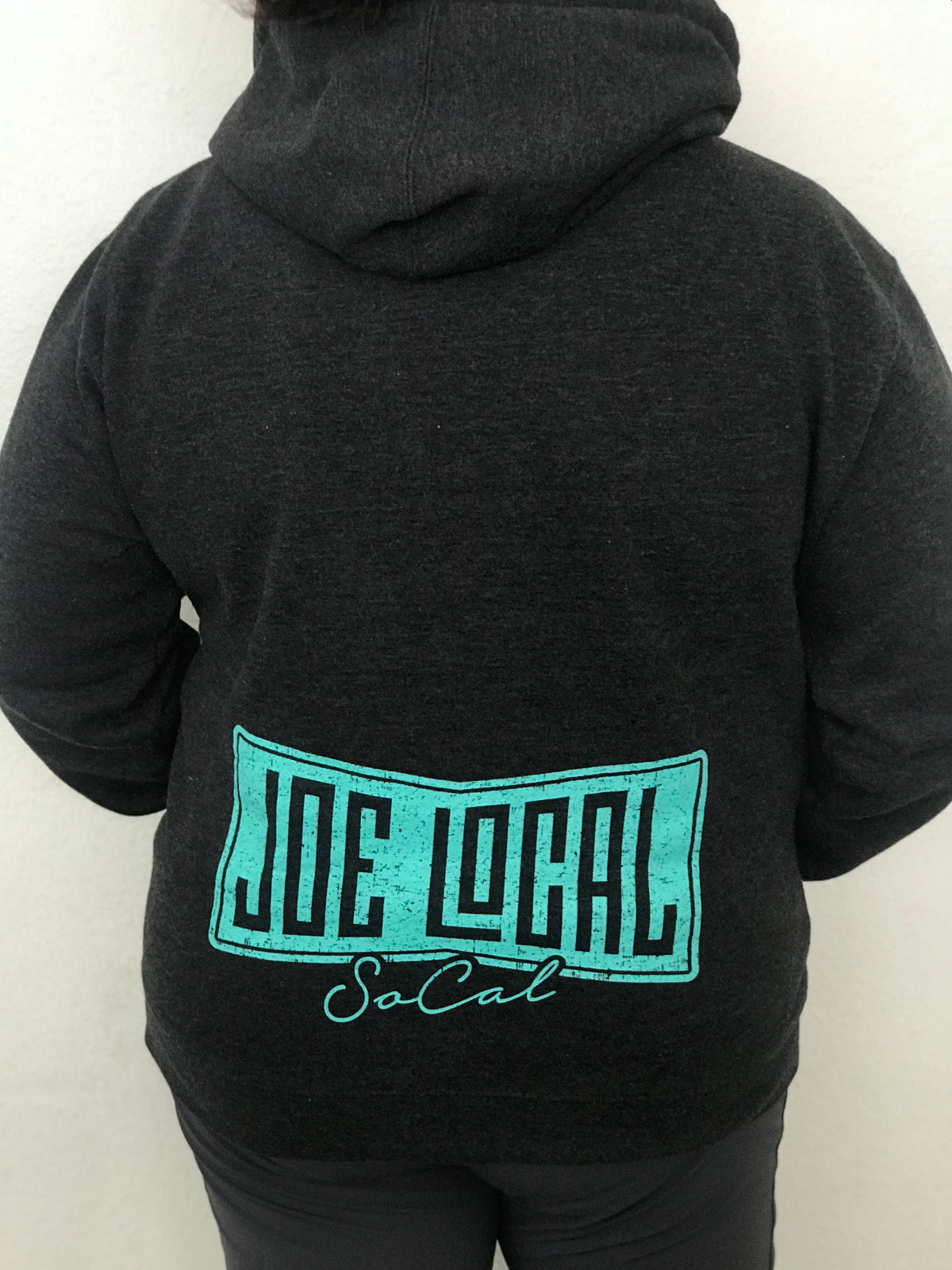 Women's mid-weight hoodie in dark gray. Joe Local mint green logo featured on left front pocket. Details of the fabric: Dark gray in color 80% Cotton/20% Polyester. jersey lined hood. Back of hoodie features large Joe Local flag logo in mint green featured at the bottom of the hoodie.