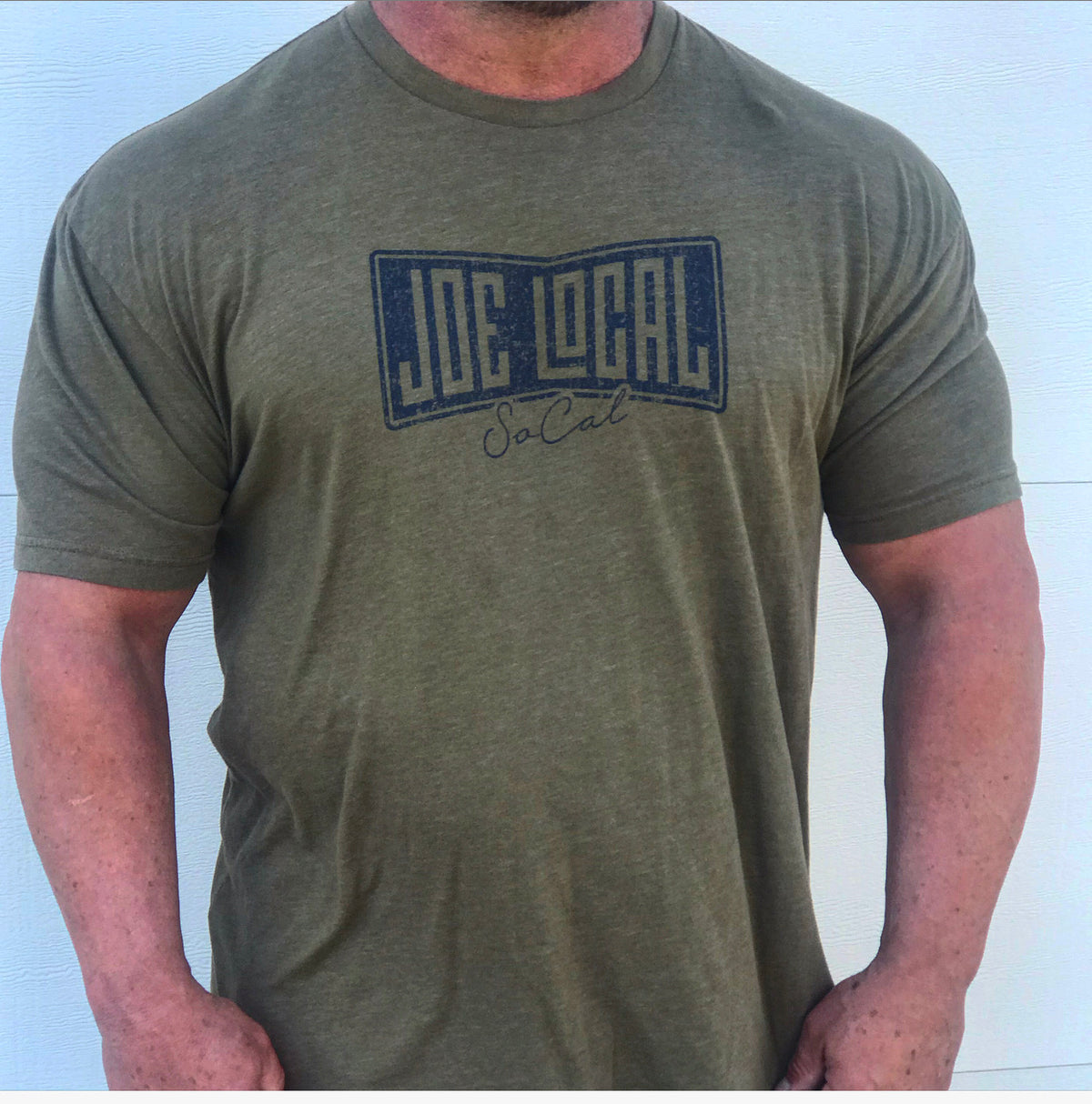 Front of the t-shirt. Military green t-shirt with navy blue Joe Local So Cal flag logo at the center of the chest. Well-fitted and comfortable t-shirt. Fabric: CVC Jersey 60% Combed Ring-Spun Cotton 40% Polyester /32 singles, 145 grams/4.3 oz Neck: Crew